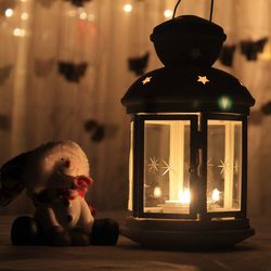 Close-up of burning tea light in lantern by toy at home