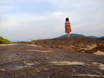 Rear view of girl standing on rock against sky