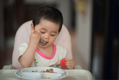 Cute baby girl eating food at home