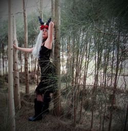 Side view of young woman standing by trees in forest