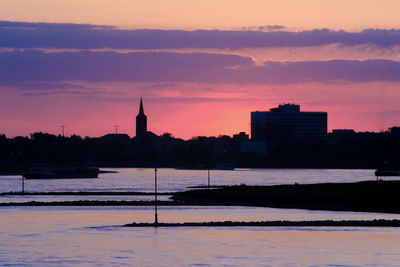 Silhouette of buildings at waterfront during sunset