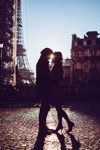 Couple standing by canal in city against sky