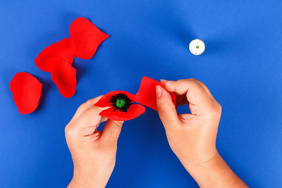 Midsection of person holding red chili pepper against blue background