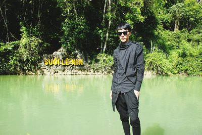 Portrait of woman standing by lake against trees