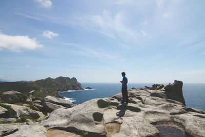 Rear view of man standing on rock by sea against sky