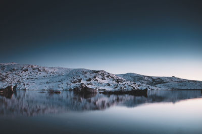 Scenic view of lake by snowcapped mountains against clear sky