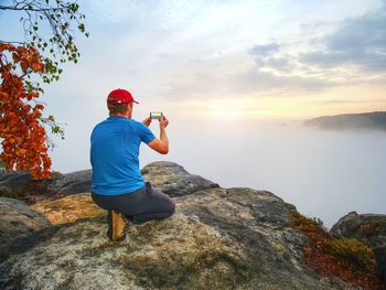 Rear view of man on rock against sky during sunset