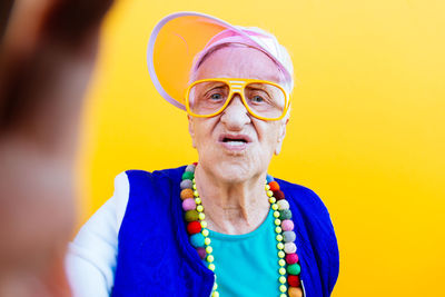 Portrait of angry senior woman standing against yellow background