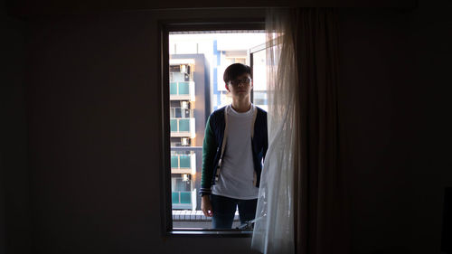 Portrait of teenage boy standing against window