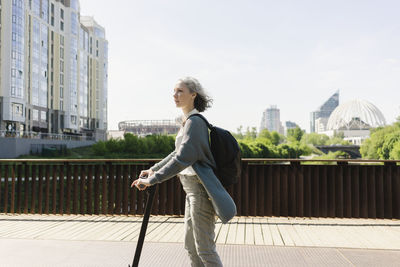 Woman with backpack riding push scooter on sunny day