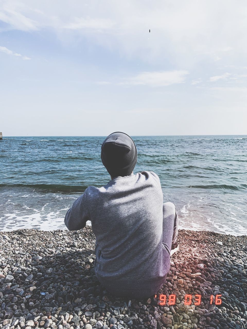 REAR VIEW OF MAN SITTING AT BEACH