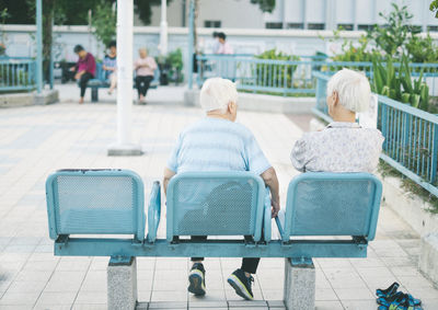 Rear view of people sitting on bench in city