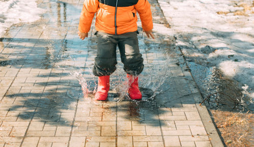 Gleeful puddles, red boots send cascade of droplets, celebration of melting snow on sunny day