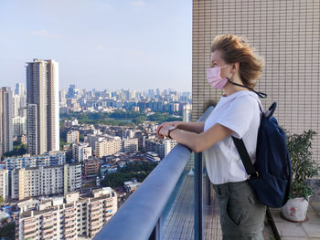 Rear view of woman looking at modern buildings in city from the roof top