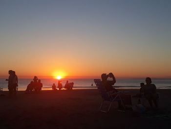 Silhouette people on beach against clear sky during sunset