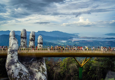 Group of people on bridge against cloudy sky