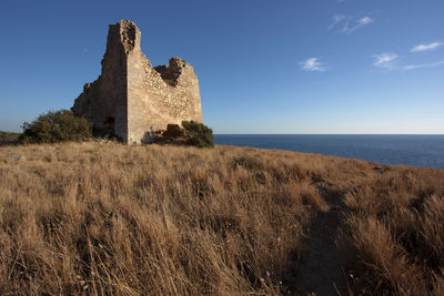 Castle on cliff by sea against blue sky