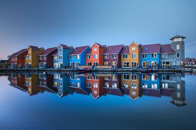 Reflection of buildings on lake against blue sky