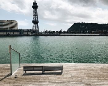 View of empty bench by water against cloudy sky