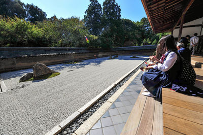 Rear view of woman sitting by plants against sky