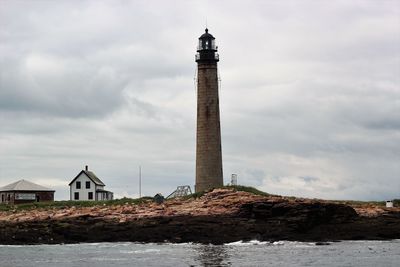 Lighthouse by building against cloudy sky