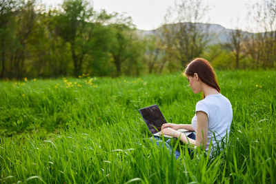 Young woman using mobile phone while sitting on field