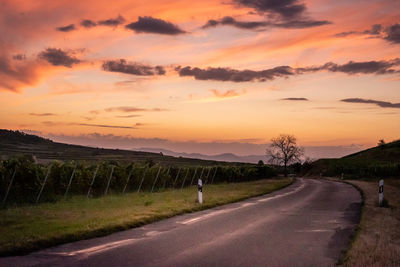 Road amidst field against sky during sunset