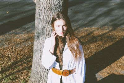 Portrait of young woman standing on tree trunk