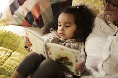 High angle view of grandmother reading book to granddaughter on bed at home