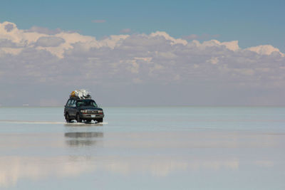 Off-road vehicle in water at salar de uyuni against cloudy sky