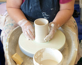 Midsection of woman sitting at potters wheel working with clay