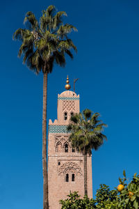 Low angle view of minaret and palm trees  against clear blue sky. 
