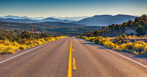 Empty road along trees and mountains against clear sky