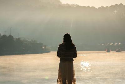 Asian woman tourist standing alone look at view at lakeside of ban rak thai village with fog on lake 