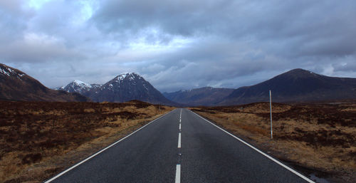 Empty road leading towards mountains against cloudy sky