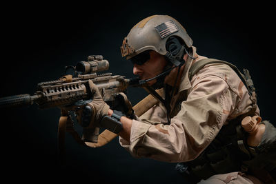 Man wearing helmet holding rifle against black background