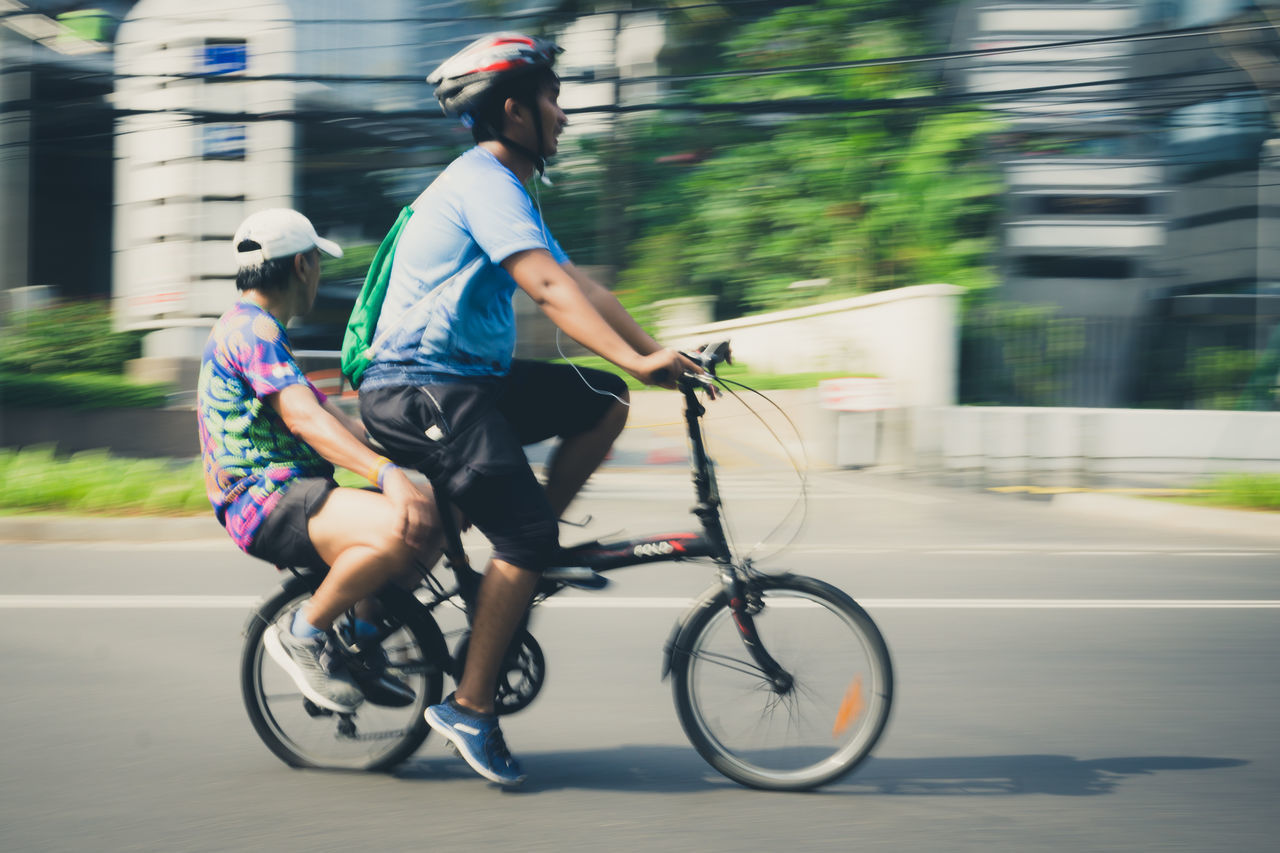 transportation, ride, bicycle, riding, motion, real people, lifestyles, sport, land vehicle, city, two people, street, blurred motion, men, women, cycling, mode of transportation, road, helmet, leisure activity, outdoors