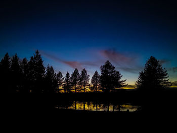 Silhouette trees by lake against sky at night