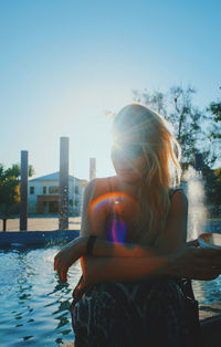 Young woman by swimming pool against clear sky
