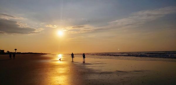 Silhouette people on beach against sky during sunset