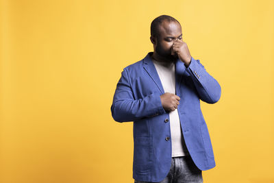 Side view of young man standing against yellow background