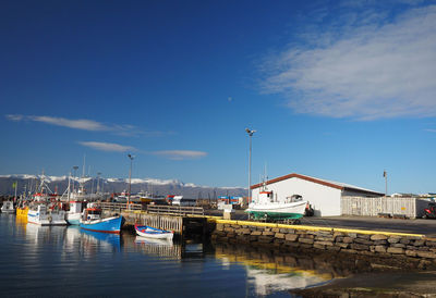 Boats moored at harbor against blue sky