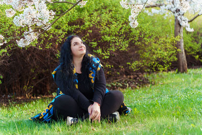 Plus size woman in blue and yellow vest admiring beauty of cherry blossom trees in park in spring