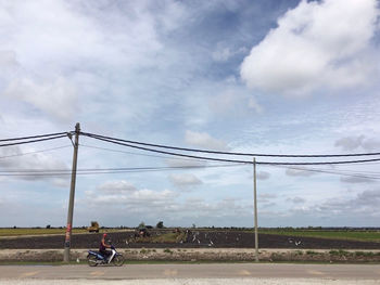 People riding motorcycle on field against sky