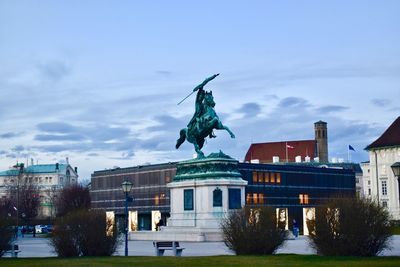 Statue amidst buildings in city against sky