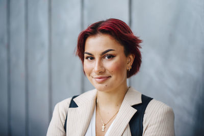 Portrait of female college student smiling against gray wall