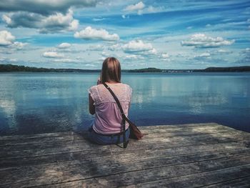 Rear view of woman sitting on pier over lake