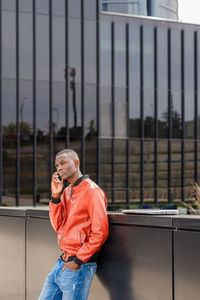 Self assured young african american guy in trendy clothes having phone conversation and looking away with attention while standing on city street in downtown on sunny day