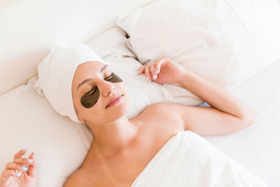 High angle view of young woman with patches under eyes lying on bed at home