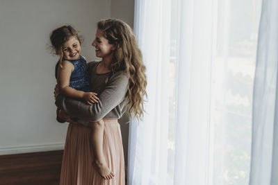 Side view of daughter being held by mother while laughing in studio